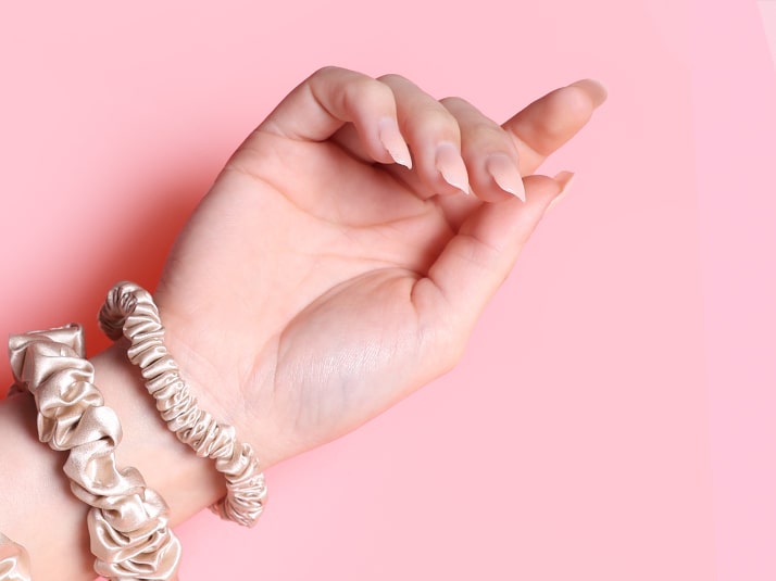 Model Wearing Champagne Hair Tie and Midi Scrunchie on wrist With Pink Background