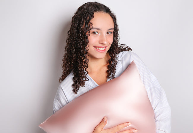 Model with curly hair holding a pink silk pillowcase