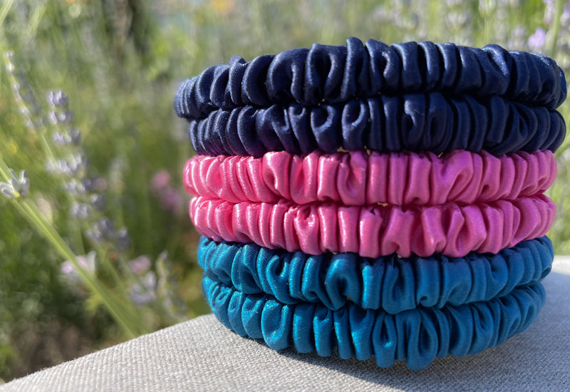 Stack of pink, blue and navy silk hair ties in front of lavender