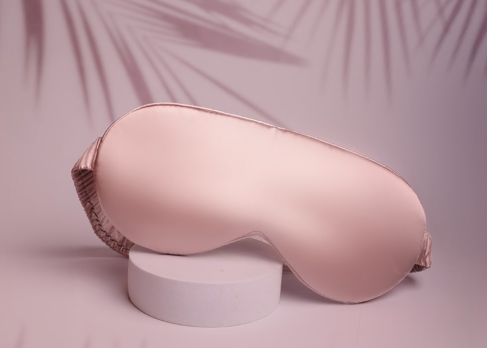 Mulberry Silk Eye Mask For Sleeping in Rose Gold Against A Pink Backdrop With Palm Leave Shadows