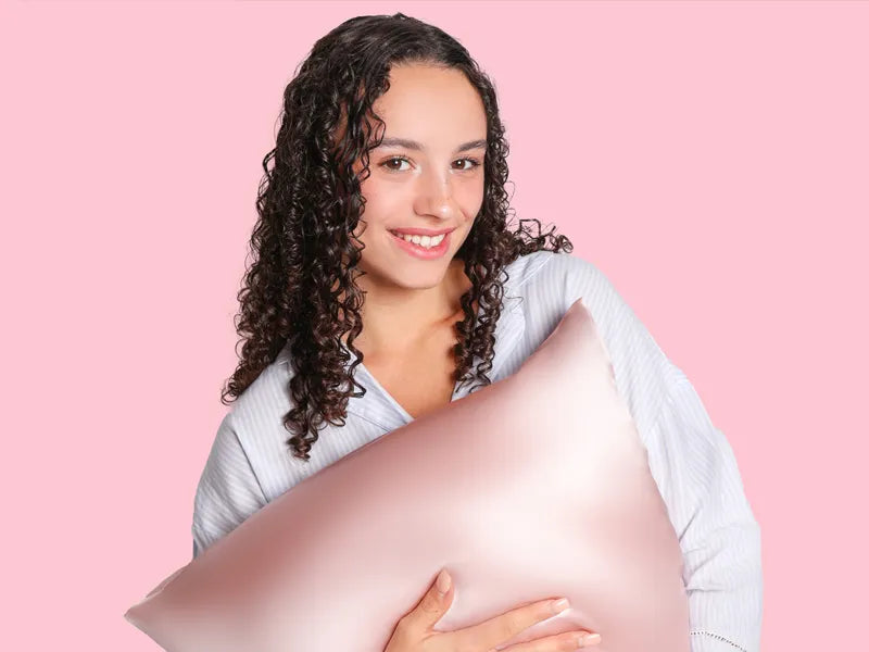 Benefits of silk pillowcases for curly hair - model with defined curls holding pink silk pillowcase