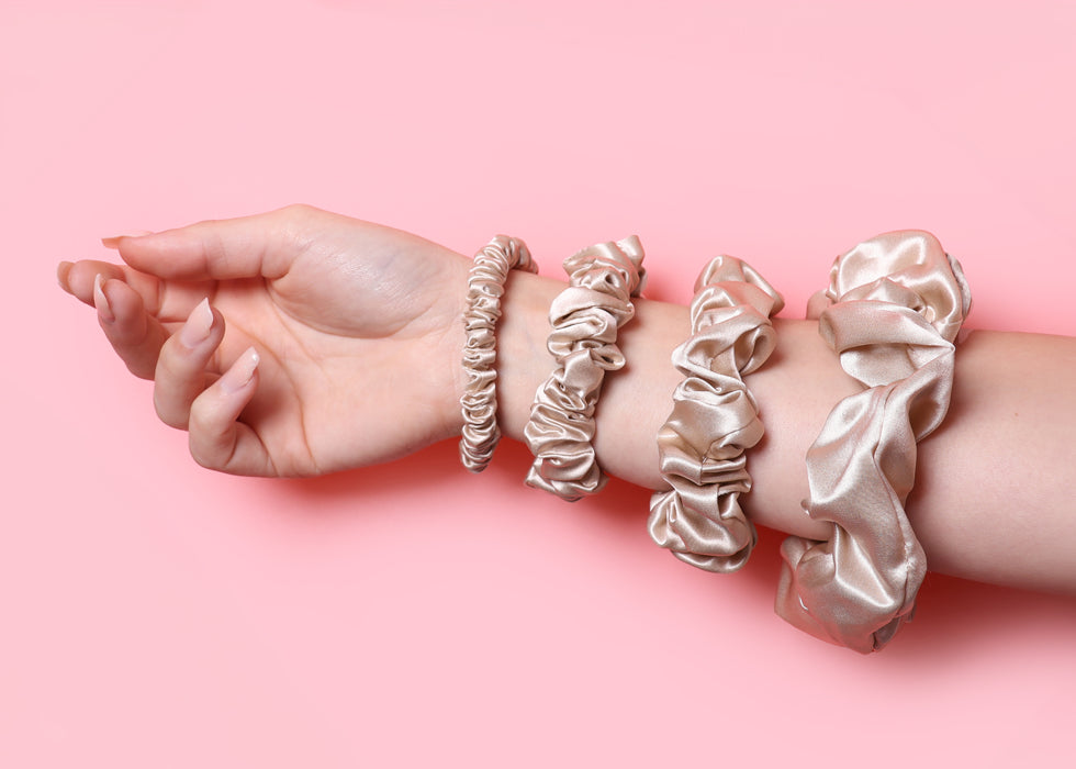 Set of silk hair ties and scrunchies on model's wrist with pink background