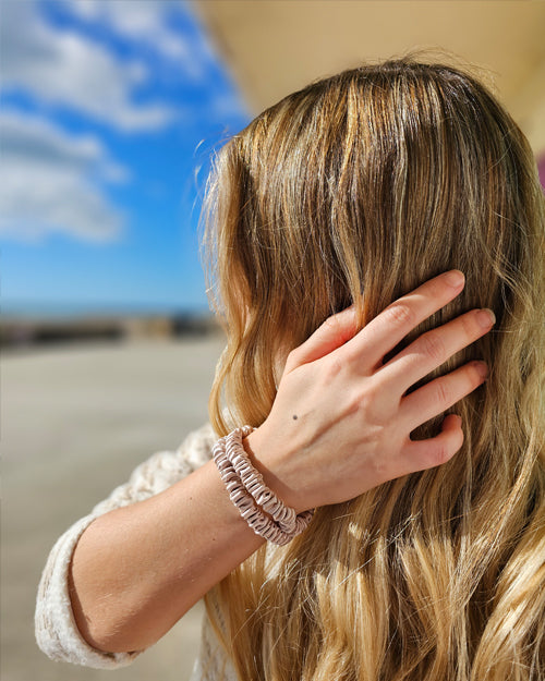 Model with long blonde hair wearing 2 pink silk hair ties on her wrist